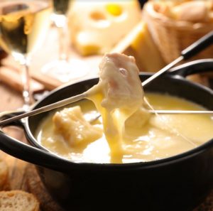 fondue a bowl of melted cheese, with bread on a skewer